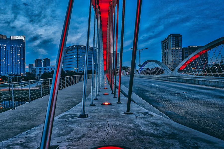 A bridge with red lights along its arches in Fort Worth, Texas, at dusk with office buildings in the background