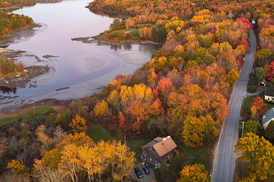 An aerial view of fall foliage in beautiful orange, reds, and yellows along a river in Maine.