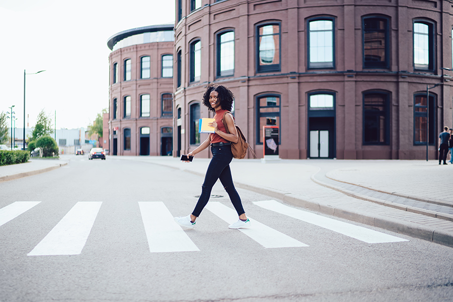Young black woman crosses the street using a painted pedestrian crossing with commercial buildings in the background