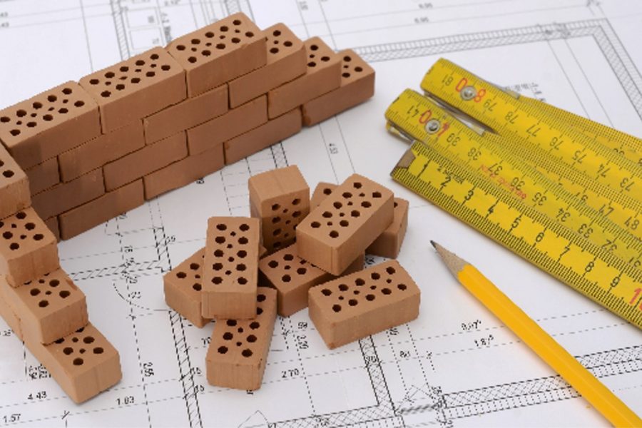 Wooden building blocks, rulers, and a pencil sit on a real estate development plan drawing