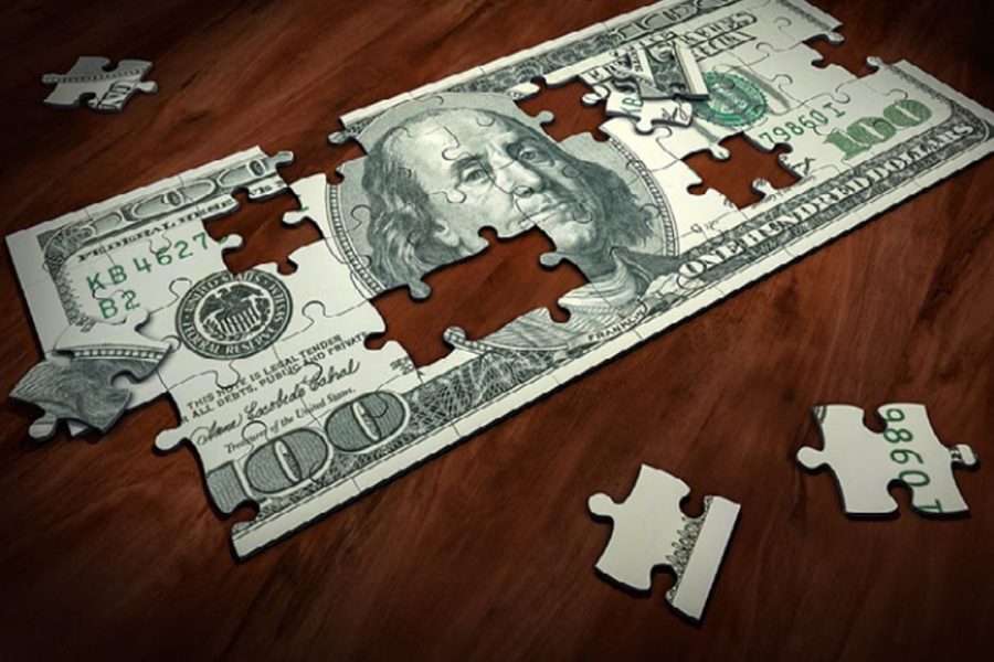 A mostly-completed puzzle that looks like a US 100 dollar bill sits on a wooden table with a few loose pieces scattered next o it