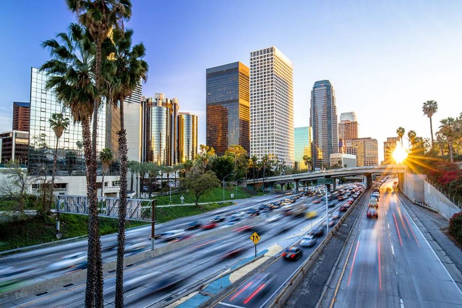 A view of the Los Angeles skyline with palm trees in the foreground and cars in motion on the freeway