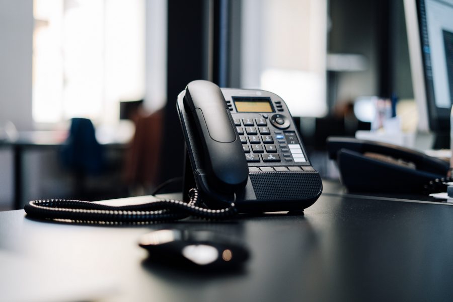 A black corded office phone sits on a desk in an office