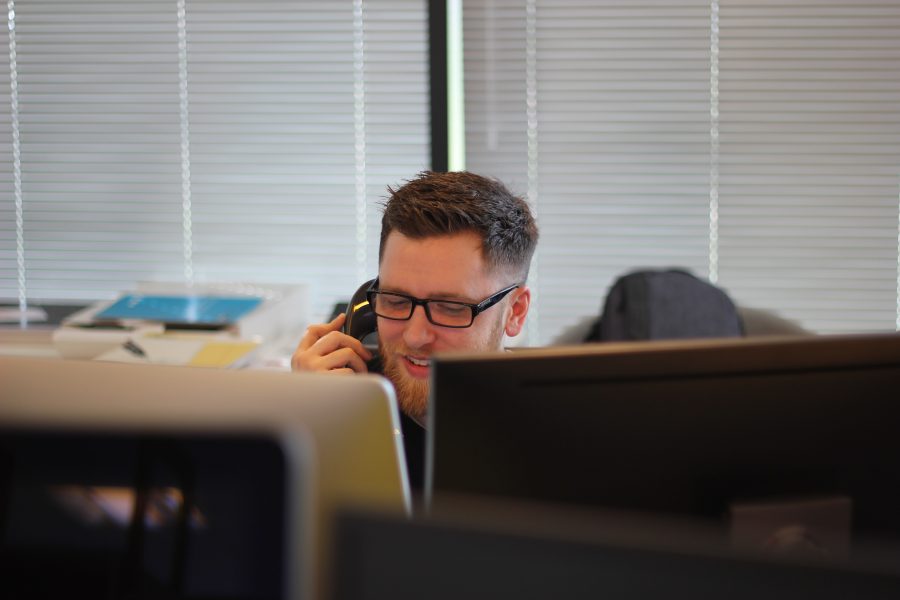 A young man sitting in front of a computer speaks with a prospect on the phone