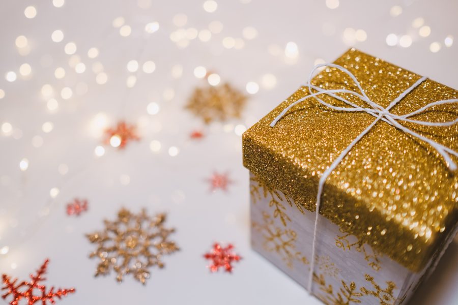 A sparkly wrapped Christmas gift tied in white string sits on a table covered by a cloth featuring multicolored snowflakes