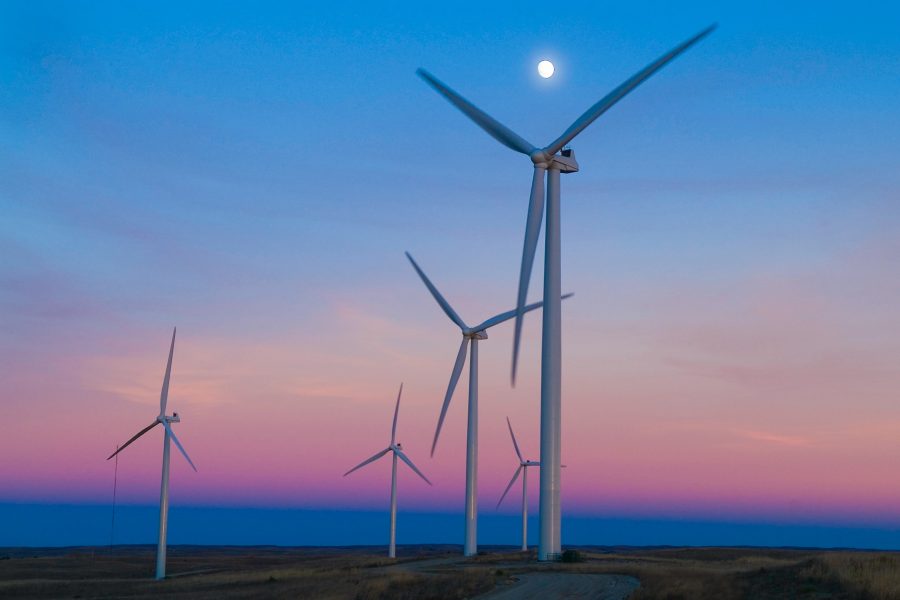 Multiple wind turbines on and open plateau in front of a beautiful blue, pink, and orange sunset with a full moon glowing above them
