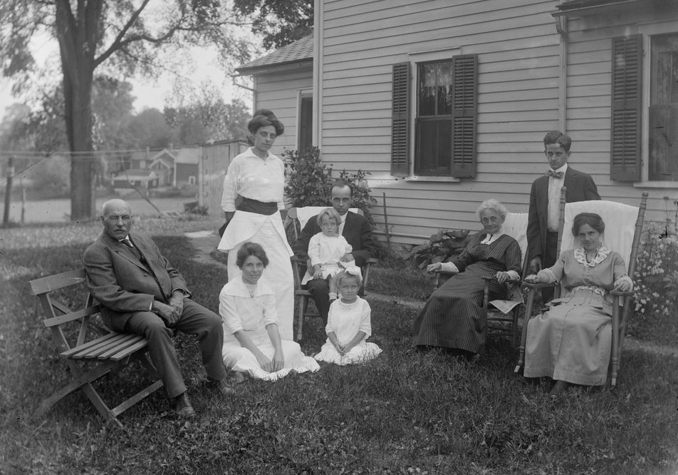 A historical photo taken in the late 1800s of three generations of family members in front of the house they shared in Massachusetts