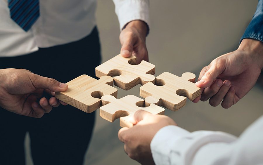 A group of people representing the people and organizations that help attract and retain businesses and workers face each other while holding separate puzzle pieces.