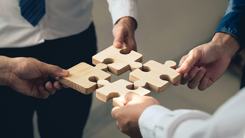 A group of people representing the people and organizations that help attract and retain businesses and workers face each other while holding separate puzzle pieces. 