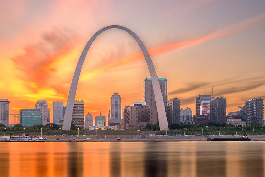 The skyline of the City of Saint Louis at sunset, looking west from the Mississippi River, shows the Gateway Arch, tall skyscrapers, and other buildings in the main downtown area.
