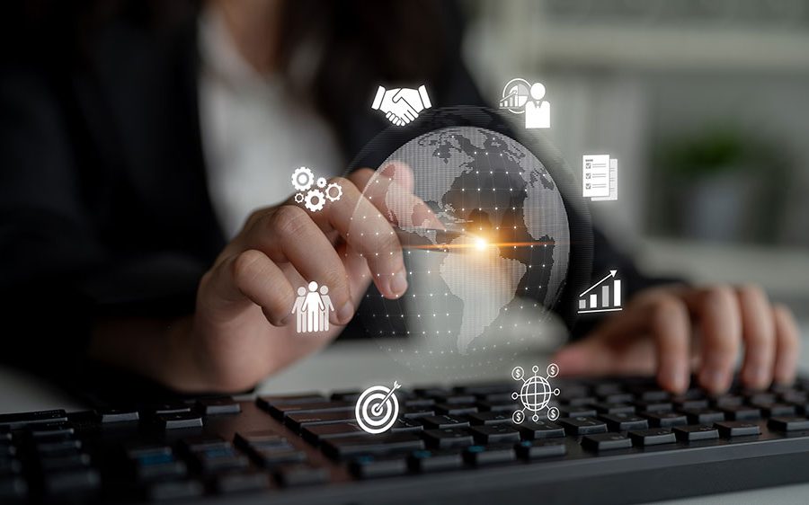 A person sits at a computer with an image of the Earth floating in front of her. She uses a digital pen to point at a spot on the Earth in South America. Icons representing lead generation, prospecting, data, investments, and meetings surround the image of the Earth.