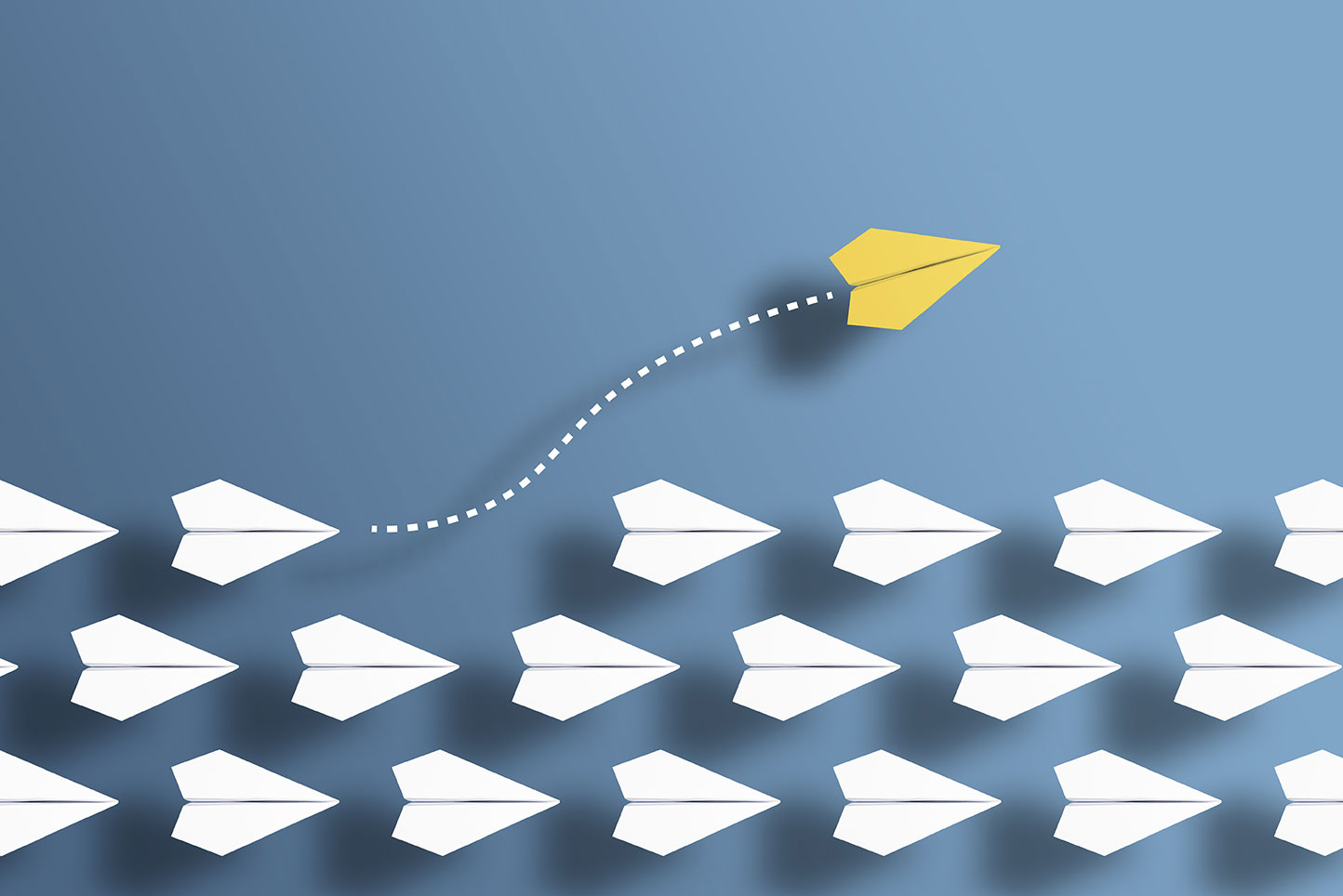 Three rows of white paper airplanes fly in tight formation, except for one yellow paper airplane that has exited the formation and gone in a different direction