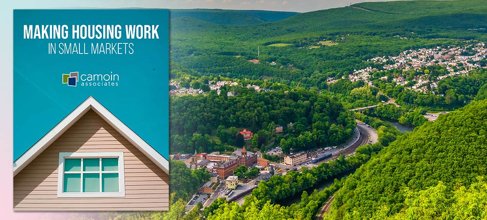 An aerial photo of a small town in the middle of a vast evergreen forest in Vermont with the cover image of the "Making Housing Work in Small Markets" white paper on top of it