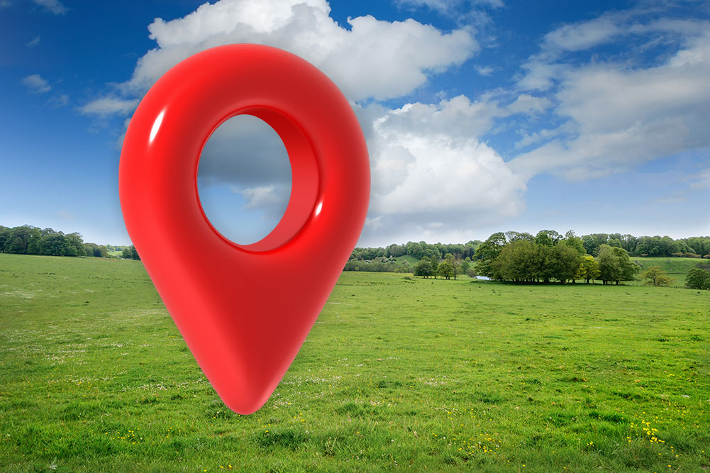 A large red map pin sits on a piece of vacant land in a rural area