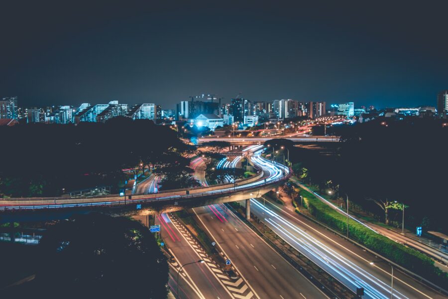 An aerial image shows an unknown city skyline at night, with a freeway interchange in the foreground and a large group of city buildings and skyscrapers in the background